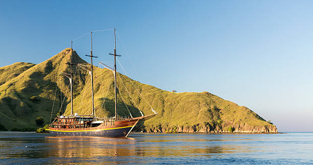 A wooden yacht with three masts is anchored in the waters of the famous archipelago of Komodo in Indonesia. The National Park of Komodo attracts numerous diving expeditions as it is considered one of the best diving destination in the World. - komodo island boat tour