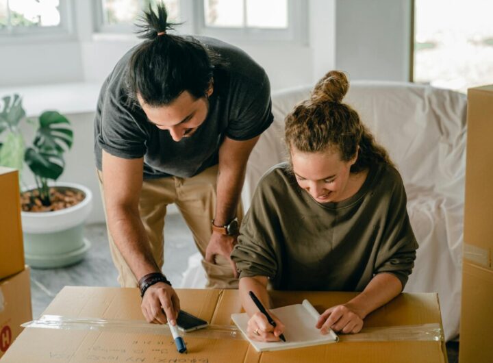 Cheerful diverse couple writing in notebook near boxes before relocation